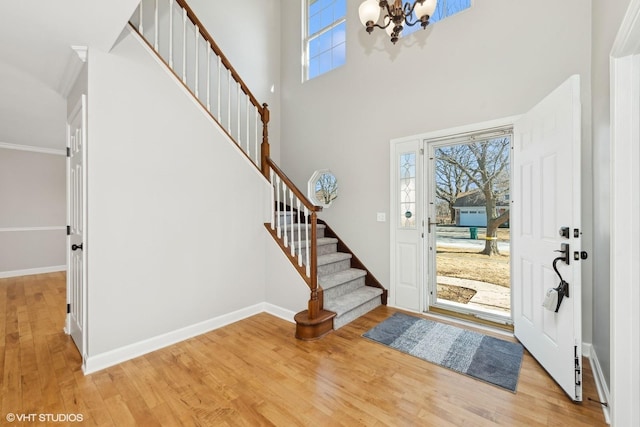 entrance foyer featuring an inviting chandelier, a towering ceiling, ornamental molding, and light hardwood / wood-style floors