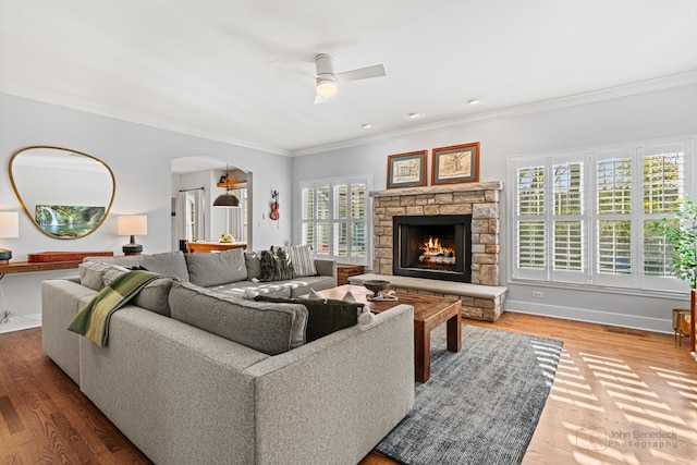 living room featuring crown molding, a stone fireplace, hardwood / wood-style floors, and ceiling fan