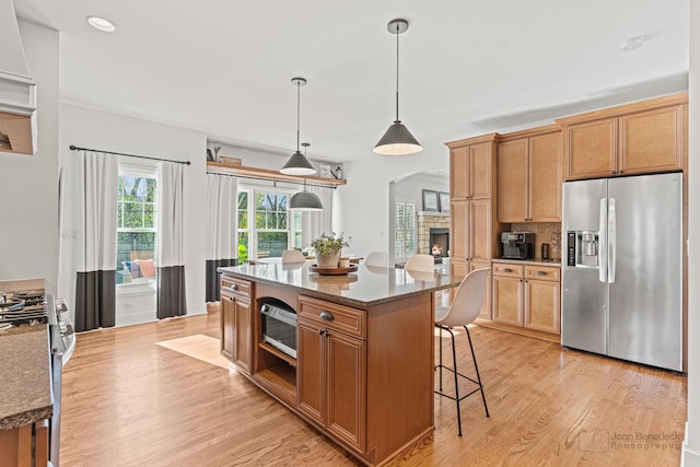 kitchen featuring stone counters, a kitchen island, hanging light fixtures, stainless steel appliances, and light hardwood / wood-style flooring