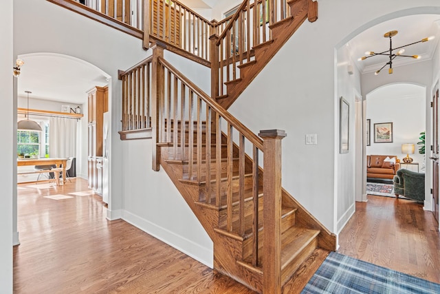 staircase with a notable chandelier, a towering ceiling, and wood-type flooring