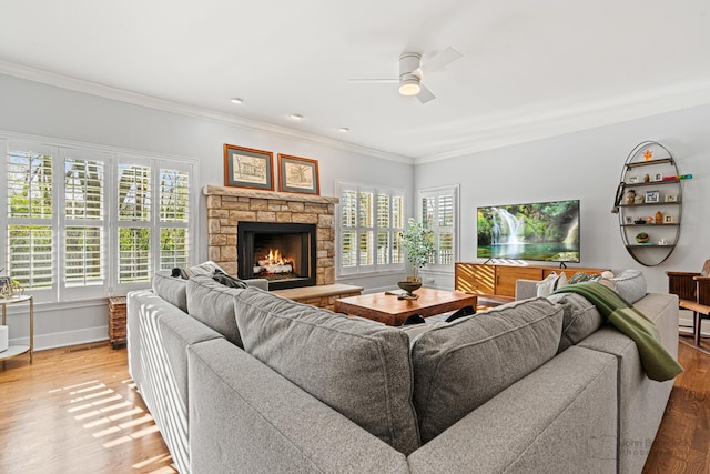 living room featuring crown molding, wood-type flooring, a stone fireplace, and ceiling fan