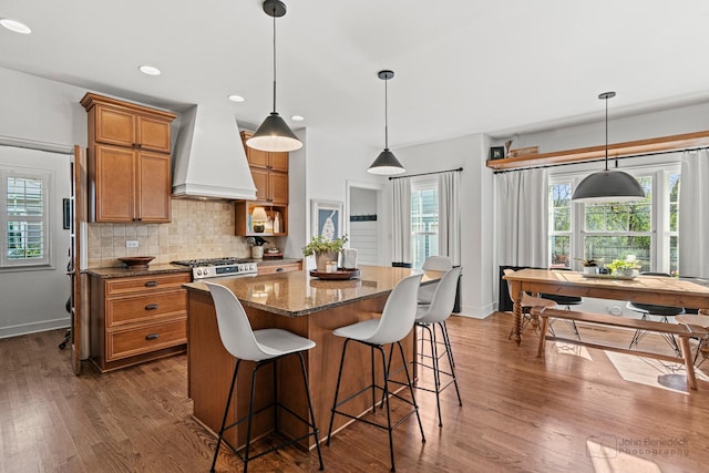 kitchen featuring range, hanging light fixtures, custom range hood, dark hardwood / wood-style flooring, and decorative backsplash