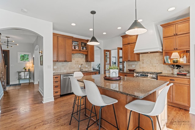 kitchen featuring premium range hood, a kitchen island, appliances with stainless steel finishes, decorative light fixtures, and dark stone counters