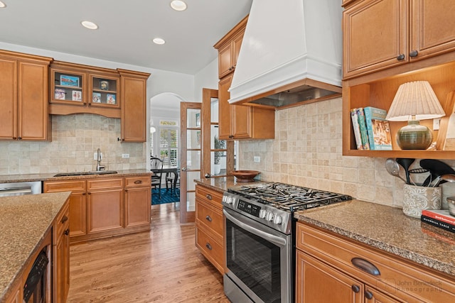 kitchen featuring sink, custom exhaust hood, stainless steel gas range oven, stone countertops, and light hardwood / wood-style flooring