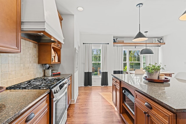 kitchen with premium range hood, hanging light fixtures, dark stone countertops, appliances with stainless steel finishes, and light hardwood / wood-style floors