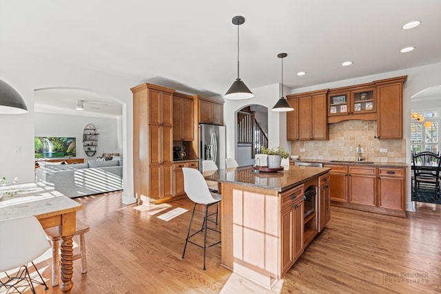 kitchen featuring sink, dark stone countertops, hanging light fixtures, stainless steel refrigerator with ice dispenser, and a kitchen island