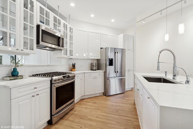 kitchen with sink, white cabinetry, stainless steel appliances, light stone counters, and decorative light fixtures