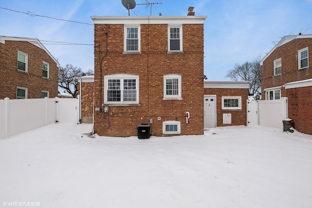 snow covered property with brick siding, a chimney, fence, and central air condition unit