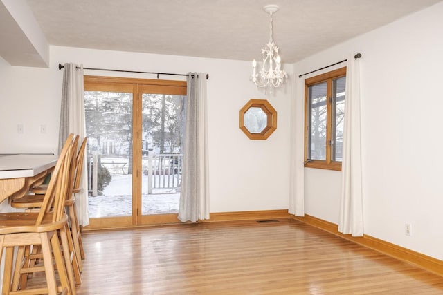 unfurnished dining area featuring plenty of natural light, light hardwood / wood-style floors, and an inviting chandelier