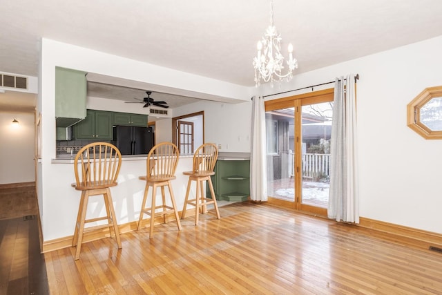 kitchen featuring black refrigerator, light hardwood / wood-style floors, a breakfast bar area, and green cabinetry