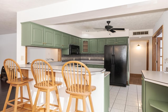 kitchen with a kitchen bar, light tile patterned floors, ceiling fan, black appliances, and decorative backsplash