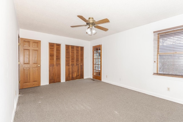 unfurnished bedroom featuring carpet, a textured ceiling, two closets, and ceiling fan