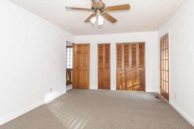 unfurnished bedroom with carpet, a textured ceiling, two closets, and ceiling fan