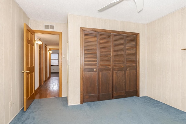 unfurnished bedroom featuring ceiling fan, dark colored carpet, a textured ceiling, and a closet