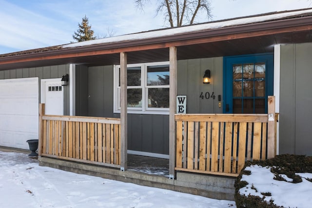 snow covered property entrance with covered porch and a garage