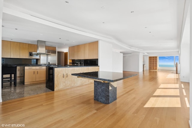 kitchen featuring island range hood, a center island, light hardwood / wood-style flooring, stainless steel microwave, and a kitchen breakfast bar