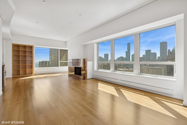 unfurnished living room with a premium fireplace, a baseboard heating unit, a wealth of natural light, and light hardwood / wood-style flooring