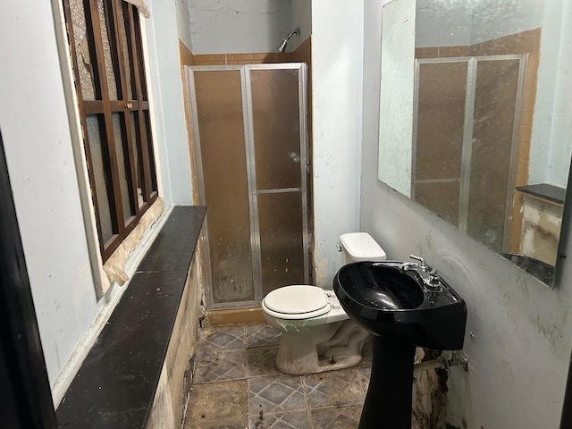 bathroom featuring toilet, a shower with shower door, and sink