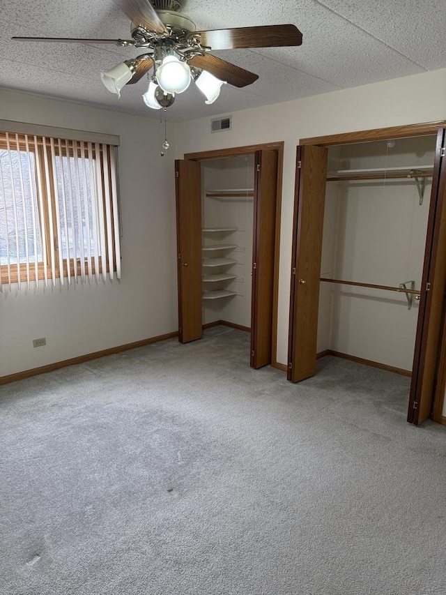 unfurnished bedroom featuring ceiling fan, light colored carpet, a textured ceiling, and two closets