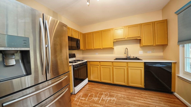 kitchen featuring light brown cabinetry, light hardwood / wood-style floors, sink, and black appliances