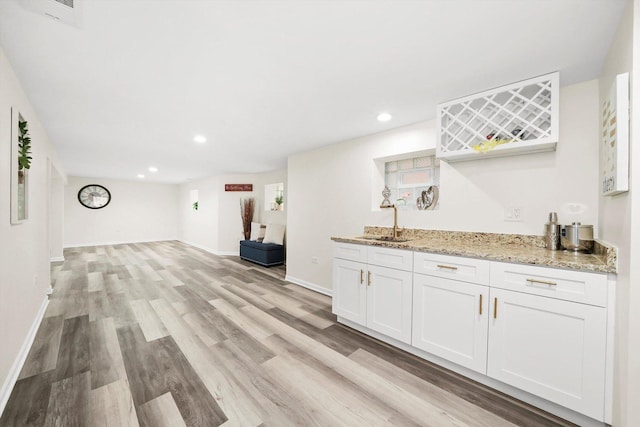 interior space featuring white cabinetry, light wood-type flooring, sink, and light stone counters