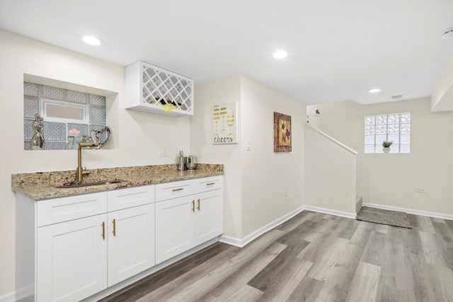 bar featuring light stone countertops, sink, white cabinets, and light hardwood / wood-style flooring