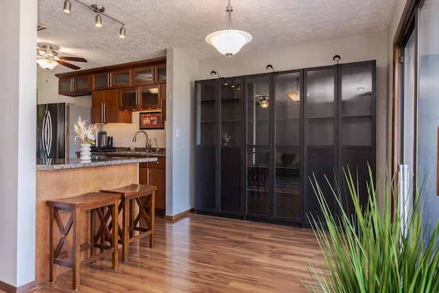 kitchen with stainless steel refrigerator, sink, dark stone counters, kitchen peninsula, and light wood-type flooring