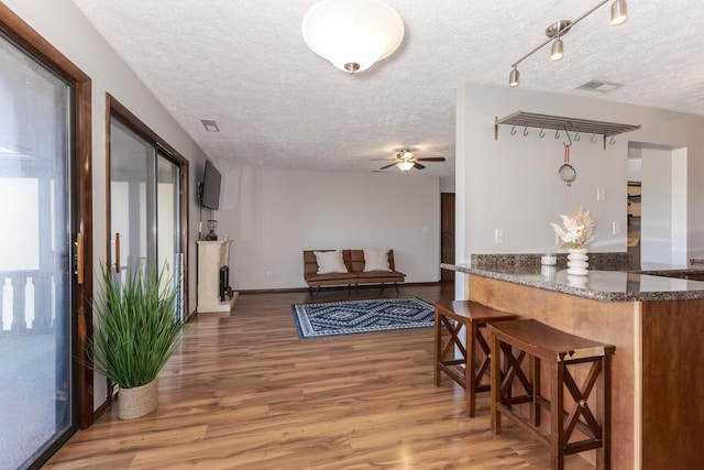 interior space featuring ceiling fan, a kitchen bar, hardwood / wood-style floors, and a textured ceiling