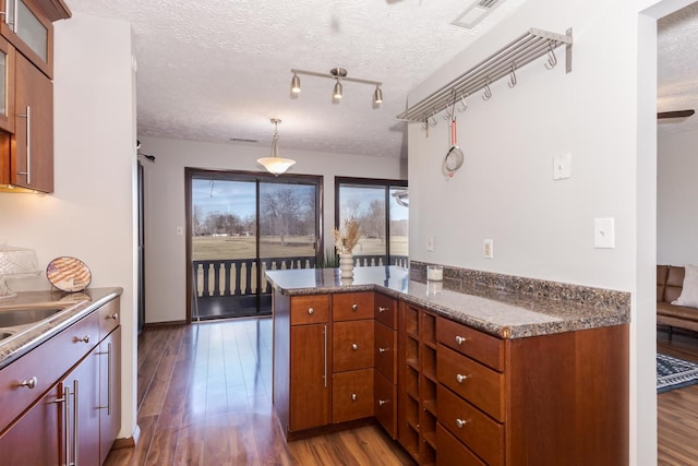 kitchen with dark stone countertops, dark hardwood / wood-style floors, a textured ceiling, decorative light fixtures, and kitchen peninsula