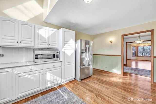 kitchen with tasteful backsplash, appliances with stainless steel finishes, light hardwood / wood-style floors, and white cabinets