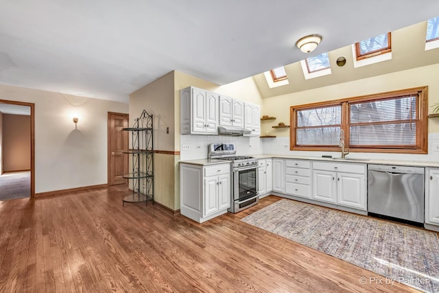 kitchen featuring sink, white cabinetry, lofted ceiling with skylight, stainless steel appliances, and light hardwood / wood-style floors