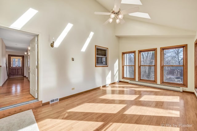 unfurnished living room with a skylight, light wood-type flooring, a wealth of natural light, ceiling fan, and a baseboard heating unit