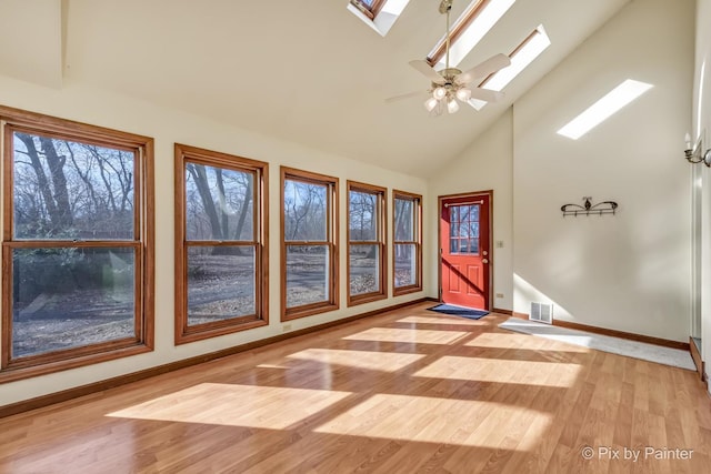 interior space featuring ceiling fan, a skylight, high vaulted ceiling, and light wood-type flooring