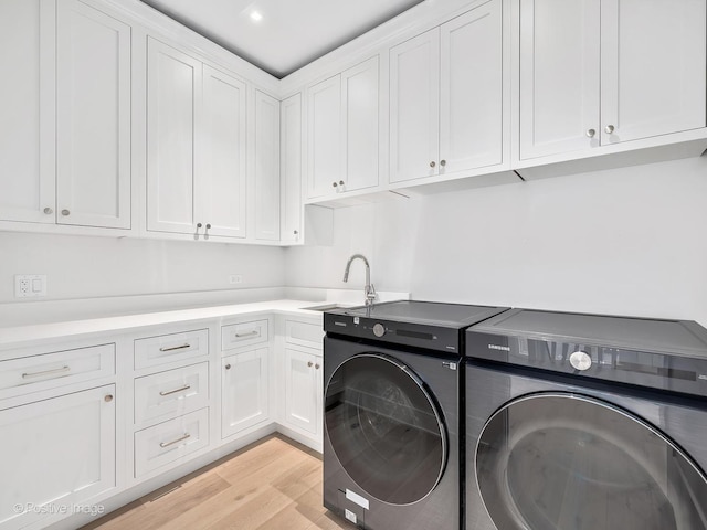 clothes washing area with cabinets, sink, washer and clothes dryer, and light hardwood / wood-style floors