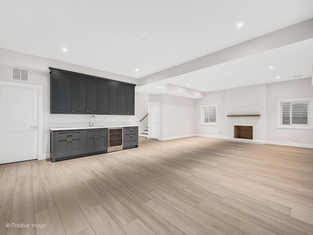 unfurnished living room with wine cooler, indoor wet bar, light hardwood / wood-style floors, and a brick fireplace