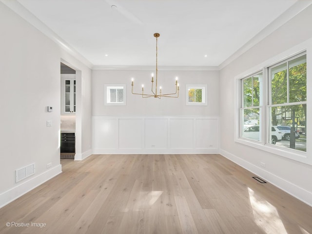 unfurnished dining area with an inviting chandelier, crown molding, and light wood-type flooring