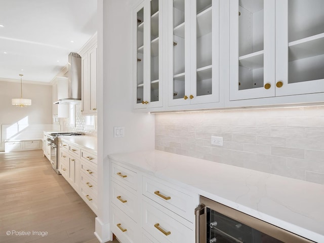 kitchen featuring pendant lighting, white cabinetry, light stone counters, stainless steel range, and wall chimney exhaust hood