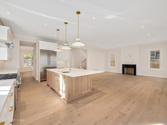 kitchen featuring sink, hanging light fixtures, high end appliances, a center island with sink, and light hardwood / wood-style flooring