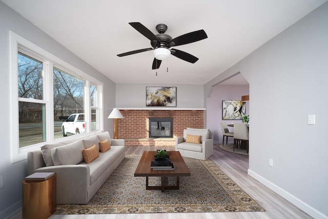 living room featuring ceiling fan, a brick fireplace, and light wood-type flooring