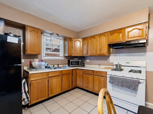 kitchen featuring sink, black fridge, a textured ceiling, light tile patterned floors, and white gas range