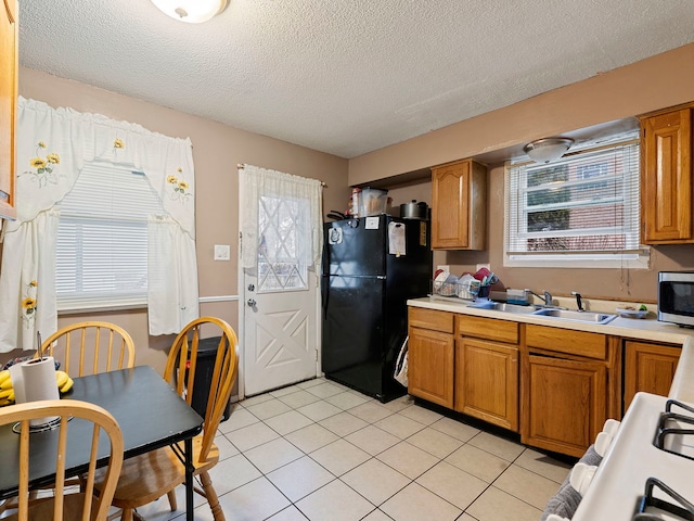 kitchen with black refrigerator, plenty of natural light, light tile patterned flooring, and sink