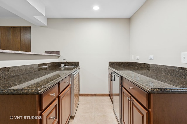 kitchen featuring dark stone countertops, light tile patterned flooring, baseboards, and a sink