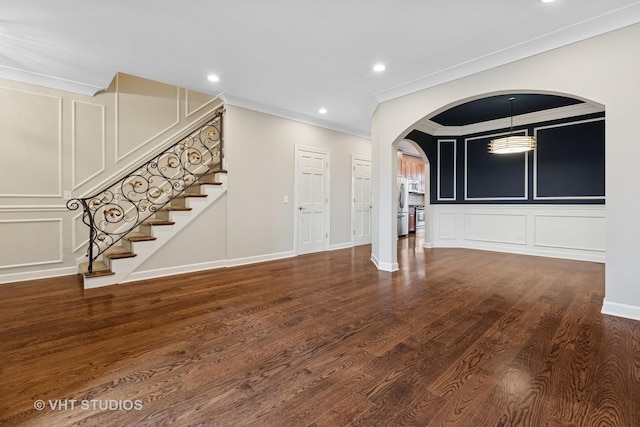 unfurnished living room with stairway, ornamental molding, wood finished floors, arched walkways, and a decorative wall