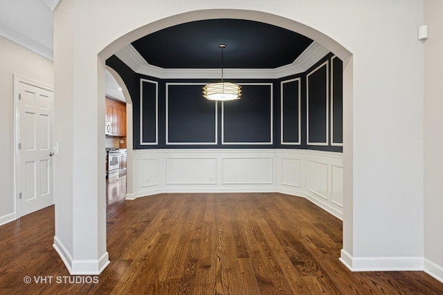 unfurnished dining area with dark wood-type flooring, baseboards, ornamental molding, arched walkways, and a decorative wall