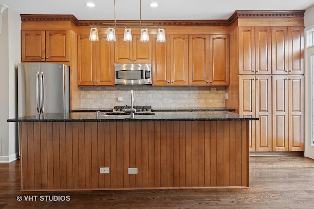 kitchen with dark wood finished floors, appliances with stainless steel finishes, dark stone counters, and an island with sink