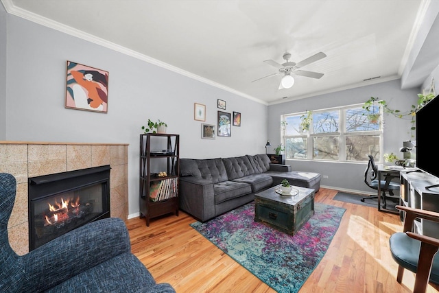 living room with a tiled fireplace, hardwood / wood-style floors, ornamental molding, and ceiling fan