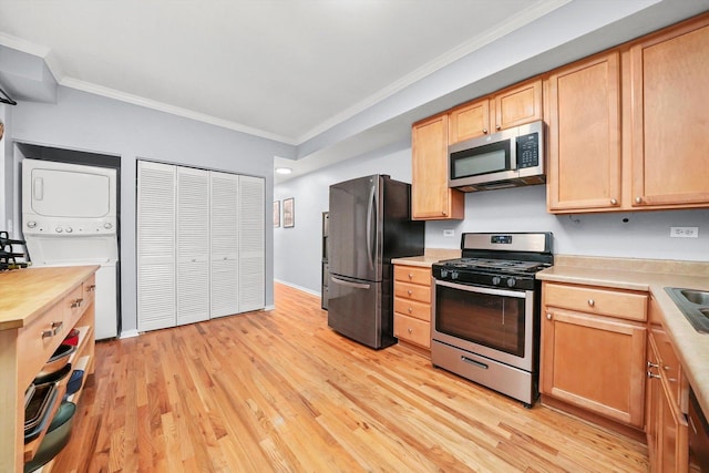 kitchen featuring stainless steel appliances, stacked washing maching and dryer, crown molding, and light hardwood / wood-style floors