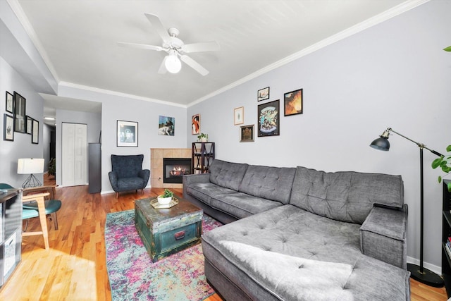 living room featuring a tiled fireplace, hardwood / wood-style floors, crown molding, and ceiling fan