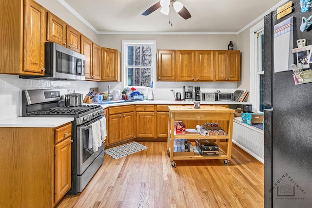 kitchen with ceiling fan, ornamental molding, stainless steel appliances, and light wood-type flooring