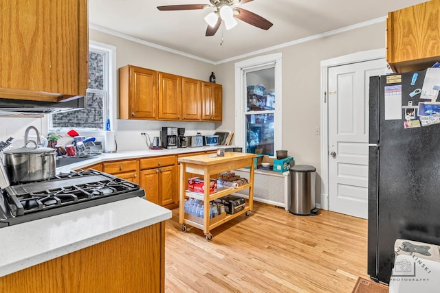 kitchen featuring range with gas stovetop, ceiling fan, crown molding, black fridge, and light wood-type flooring